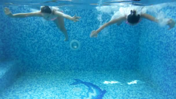 Wideo 4K z dwóch nastoletnich dziewcząt nurkowania pod wodą w krytym basenie. Dzieci bawią się i cieszą się wodą — Wideo stockowe
