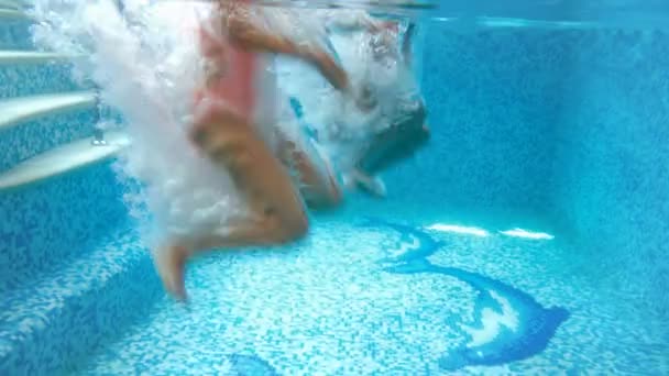 4k видео двух девочек-подростков, держащихся за руки и прыгающих в бассейн. Вид из-под воды. Дети играют и веселятся в бассейне в тренажерном зале — стоковое видео