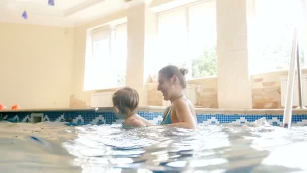 Filmagem 4k de feliz jovem mãe com o menino brincando e curtindo natação na piscina no ginásio — Vídeo de Stock