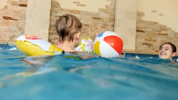 4K video av leende småbarn pojke simma i pool med uppblåsbar ring och leka med färgglada badboll — Stockvideo