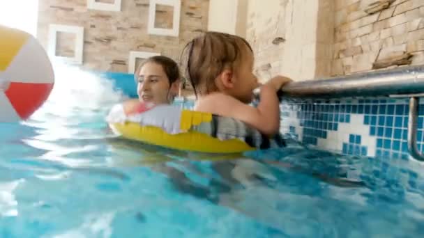 Vídeo 4k de mãe feliz com criança brincando na piscina interior com bola de praia colorida inflável — Vídeo de Stock