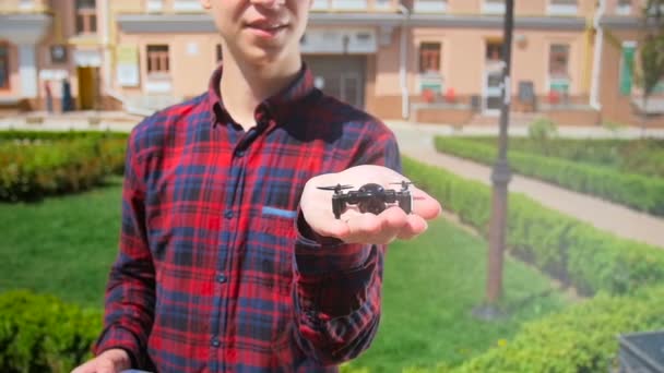 Vídeo em câmera lenta do jovem mostrando drone minúsculo para filmar vídeo ou fotografia em sua mão. Tecnologia moderna em miniatura — Vídeo de Stock