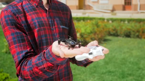 Closeup vídeo em câmera lenta de drone de brinquedo minúsculo decolando jovens homens mão no parque. Adolescente brincando com pequeno drone para tirar vídeo aéreo e fotografia — Vídeo de Stock