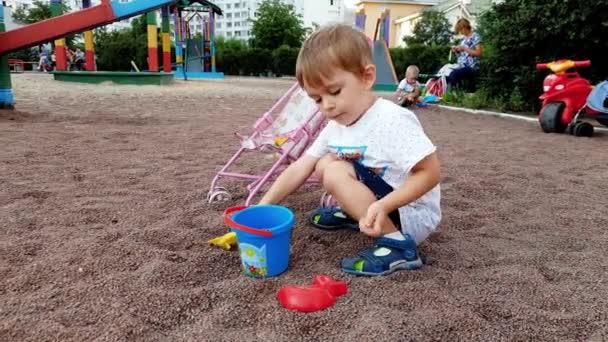 4k primer plano de vídeo de niño adorable excavación de arena con cuchara en sandbox en el parque — Vídeos de Stock