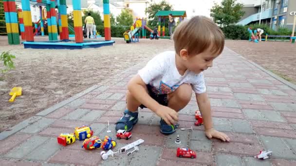 4k záběry 3 let starého batole hocha, který sedí na zemi na hřišti a hraje si s hračkářama — Stock video