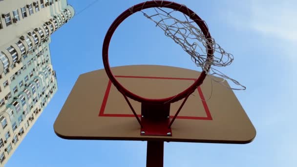 4k video del anillo de baloncesto contra el cielo azul y el edificio alto. Cesta con red para lanzar pelota en el distrito — Vídeo de stock