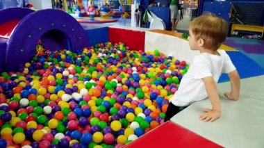 Eğlence parkında renkli plastik top dolu oyun alanında eğlenen ve oynayan küçük çocuğun 4k video