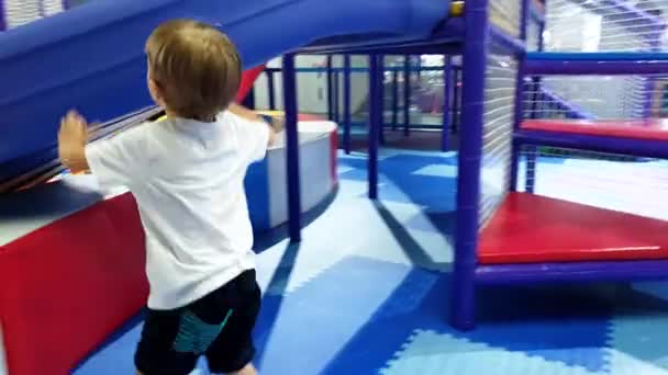 4k video de niño pequeño escalando y jugando en un patio de recreo suave en el parque de atracciones. Niños activos divirtiéndose — Vídeos de Stock