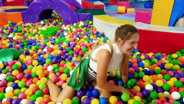 4k кадров молодой женщины упал в бассейн с цветным пластиковым мячом на детской площадке в парке развлечений — стоковое видео