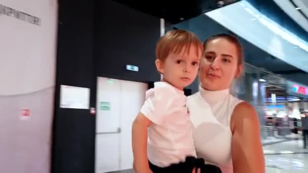 4k felvételeket a fiatal mosolygó anya gazdaság ő kisgyermek fia és a gyaloglás a bevásárlóközpontban — Stock videók