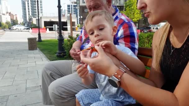 4k video of young mother, grandfather and toddler boy launching toy helicopter on bench at park — Stock Video