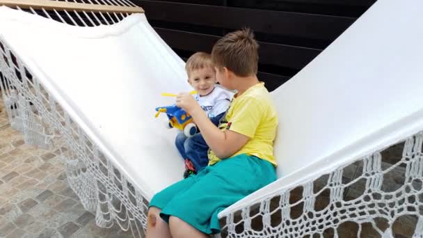 4K video av äldre bror leker med småbarn pojke på hängmattan på House Backyard — Stockvideo