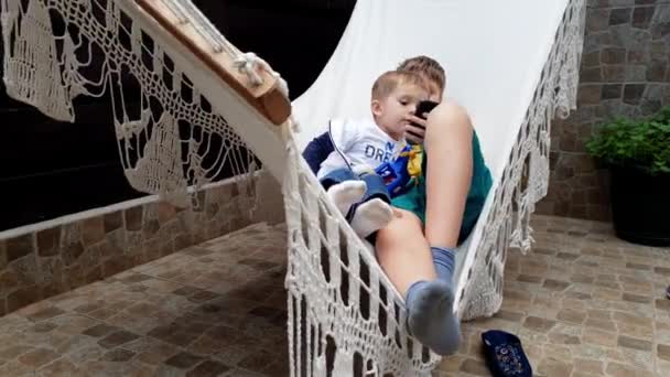 4k video van twee broers swingend in hangmat en het spelen van games op de smartphone in House achtertuin — Stockvideo