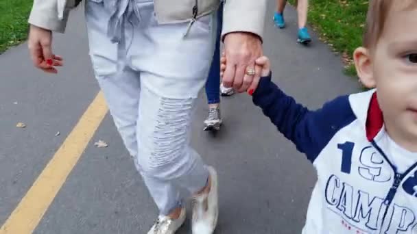 4k-beeldmateriaal van jonge moeder die haar peuter zoon met de hand houdt en op straat loopt — Stockvideo