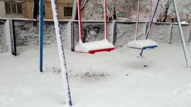 Kışın kar fırtınası ndan sonra karla kaplı oyun alanında salıncak4k görüntüleri. Etrafta çocuk oynamıyor.