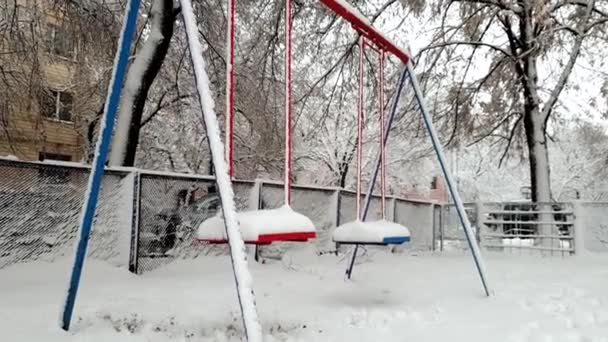 4k beelden van schommels op speelplaats bedekt met sneeuw na Blizzard in de winter. Geen kinderen spelen rond — Stockvideo