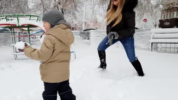 公園の遊び場で雪合戦をしている彼女の幼児の息子と若い母親の4k映像 — ストック動画