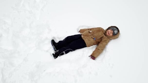 4k видео веселого игрушечного мальчика, лежащего на снегу в парке и смеющегося — стоковое видео