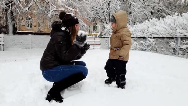 Vídeo 4k de criança rindo menino brincando com a jovem mãe no playgrund coberto de neve. Família jogando bolas de neve — Vídeo de Stock