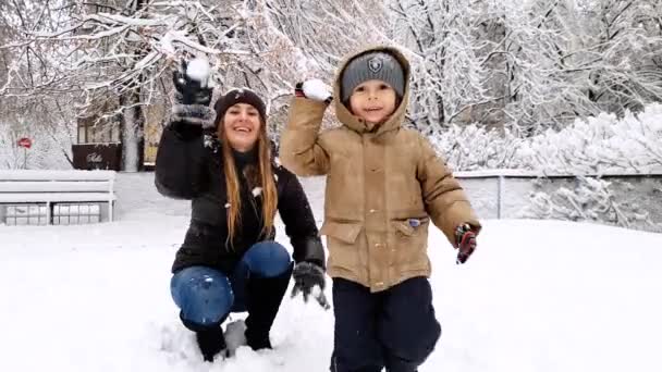 4K πλάνα της νεαρής μητέρας με το νήπιο γιο της με χιονόμπαλα αγώνα στην παιδική χαρά στο πάρκο — Αρχείο Βίντεο