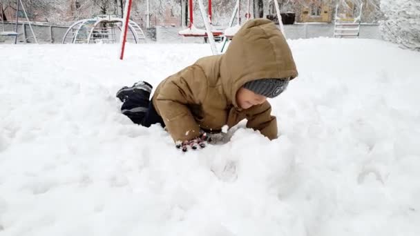 4k видео счастливого улыбающегося мальчика, играющего в зимнем парке и бросающего снежок в камеру — стоковое видео