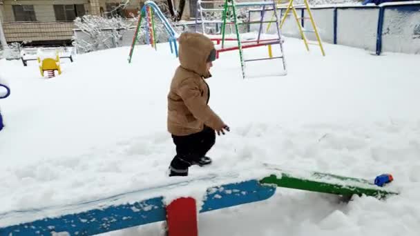 4k-beelden van peuter jongen wandelen en klimmen over sneeuw drift op de speelplaats in Park na sneeuwstorm — Stockvideo