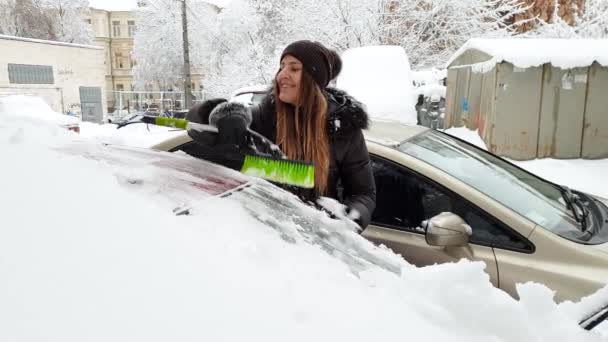 4k видео красивой женщины-водителя, чистившей свой автомобиль от снега после метели в первой половине дня — стоковое видео