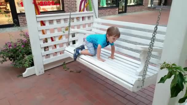 Imágenes de 4k del niño sentado en el columpio del banco en la calle de la ciudad — Vídeos de Stock