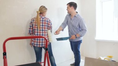Mutlu genç çift eğlenmek ve yeni evde yenileme yaparken boya silindirleri ile birbirlerine vurmak
