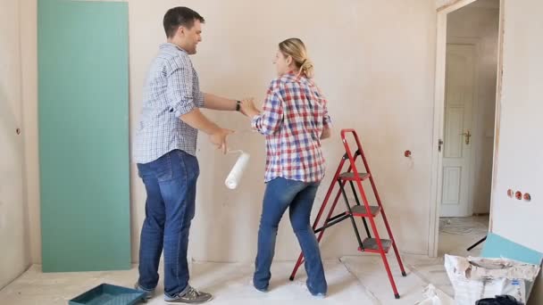 Imágenes en cámara lenta de la alegre y sonriente pareja joven y saltando mientras hacen la renovación en su nuevo apartamento — Vídeos de Stock