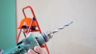 Elektrik matkabını tutan ve çalıştıran inşaat işçisi veya inşaatçının yakın çekim yavaş çekim videosu. Matkap ucu hızlı dönüyor