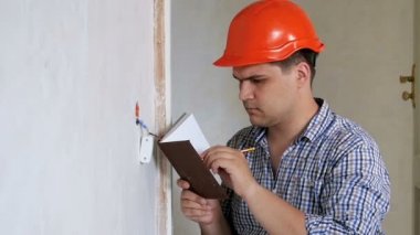 Erkek inşaat işçisi veya inşaatçının ölçüm yapıp hesaplamasını not defterine yazmasının yavaş çekim görüntüleri. İnşaat veya tadilat tasbısıaltında evde çalışan yüklenici