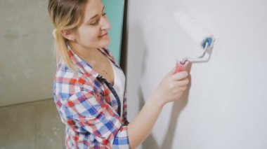 Evinde yenileme yapan damalı gömlekli güzel genç kadının videosu. Boya rulo ile duvarlar boyama genç kız