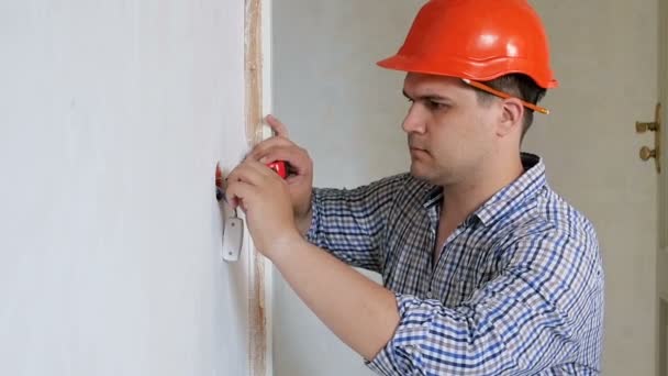Zbliżenie wideo w zwolnionym tempie męskiego budowniczego lub robotnika budowlanego do mierzenia ścian z taśmą pomiarową. Człowiek robi remont w domu — Wideo stockowe