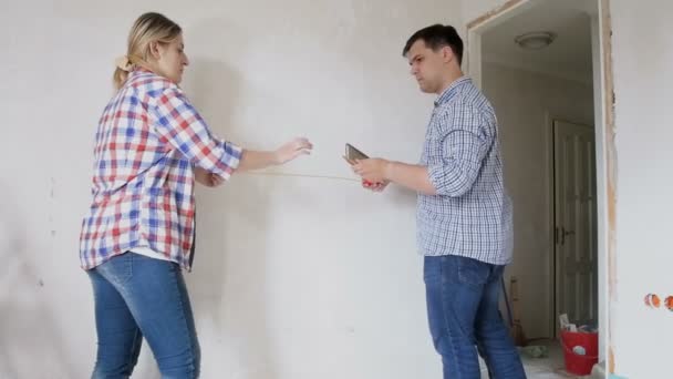 Slow motion video av ungt par mäta väggarna i sitt hem under renovering med måttband — Stockvideo