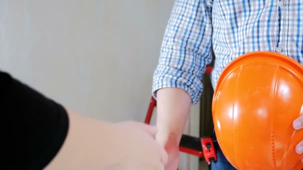 Замедленная съемка крупным планом, где молодая предпринимательница пожимает руку строителю или строительному работнику в новом доме или квартире — стоковое видео