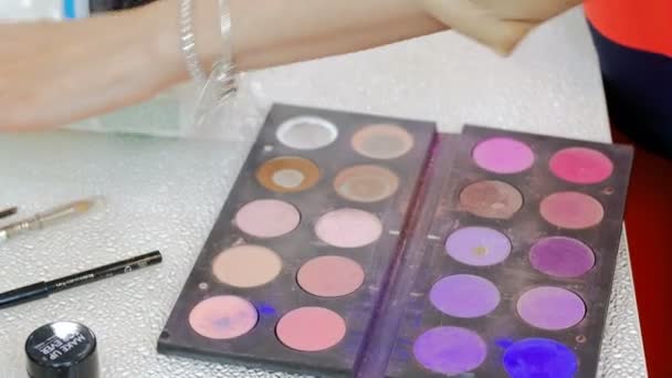 Closeup vídeo de paleta colorida com tintas e sombras para maquiagem. Artista de maquiagem profissional ou visagiste segurando paleta e escolhendo a cor certa com escova — Vídeo de Stock