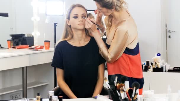 Primer plano 4k metraje de la cara de modelos de moda, mientras que el artista de maquillaje profesional aplicando rímel y sombras de ojos en la cara antes de desfile de moda — Vídeos de Stock