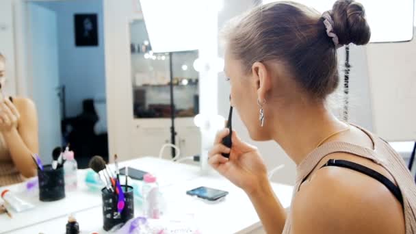 Pomalý videozáznam krásného mladého ženského módního modelu aplikováním make-upu v zrcadle ve visážním studiu — Stock video
