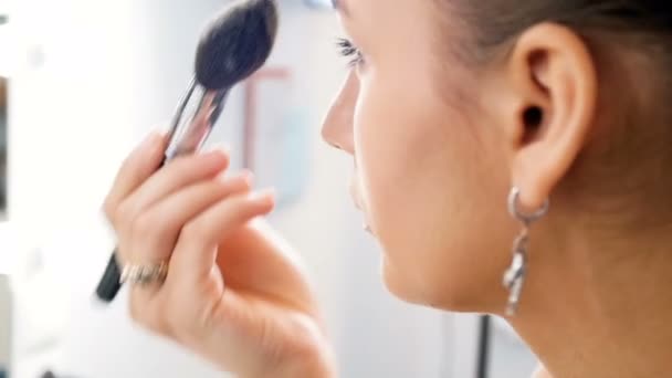 Slow motion video of beautiful young female fashion model applying makeup looking in mirror in visage studio — Stock Video