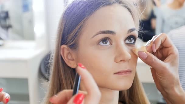 Closeup slow motion video of professional makeup artist applying cosmetics and preparing young female model for photoshooting — Stock Video