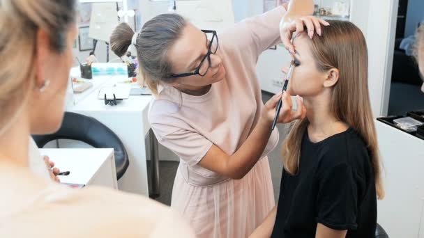 Video de la artista de maquillaje profesional femenina enseñando a sus estudiantes la aplicación de rímel, lápiz labial y tonos en la cara modelos. Mujer joven tomando clase de rostro profesional — Vídeos de Stock
