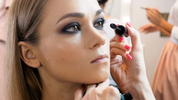 Närbild slow motion video av professionella makeup artist tillämpa kosmetika och förbereda unga kvinnliga modell för fotografering — Stockvideo