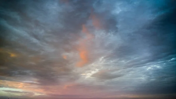 Hermosa imagen de nubes azules, anaranjadas, amarillas y rosadas en el cielo a la luz del sol puesta del sol — Foto de Stock