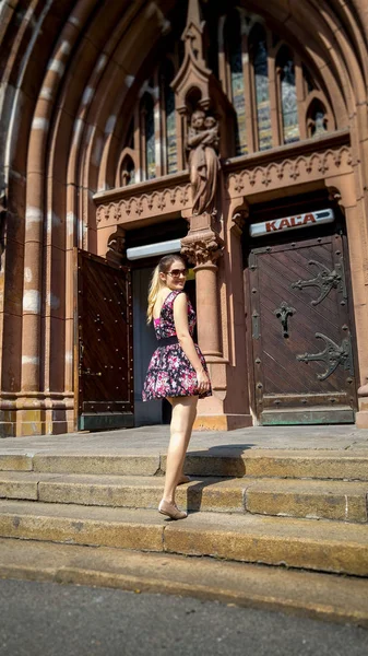 Beautiful smiling young woman posing on old stone stairs against catholic cathedral at old town — Stock Photo, Image