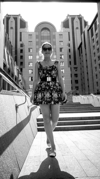 Black and white image of smiling young woman in dress walking down the stone stairs on street at bright sunny day — Stock Photo, Image