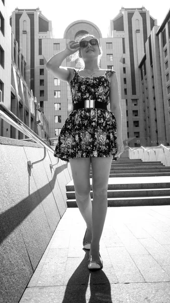 Black and white portrait of beautiful smiling young woman posing on stone stairs against modern building at bright sunny day — Stock Photo, Image