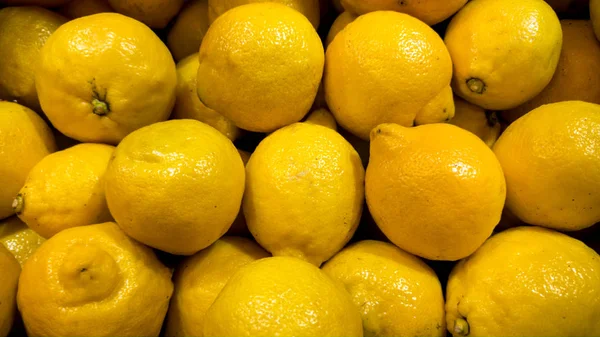 Imagen de cerca de un montón de limones orgánicos que yacen en el mostrador de la tienda. Textura de primer plano o patrón de frutas frescas maduras. Hermoso fondo de comida — Foto de Stock