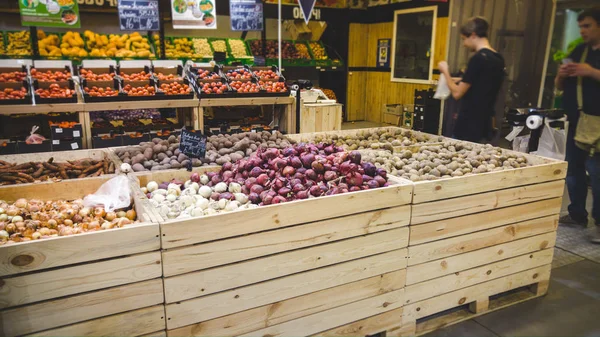 Closeup image of garlic, onions, potatoes and other fresh vegetables lying in wooden crated in grocery store — Stock Photo, Image