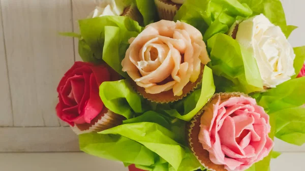 Closeup photo of flower bouquet made of cakes and cupcakes on white wooden desk. Beautiful shot of sweets and pastry over white background